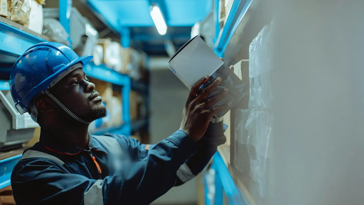 Warehouse worker in a hard hat checking stock on a shelf